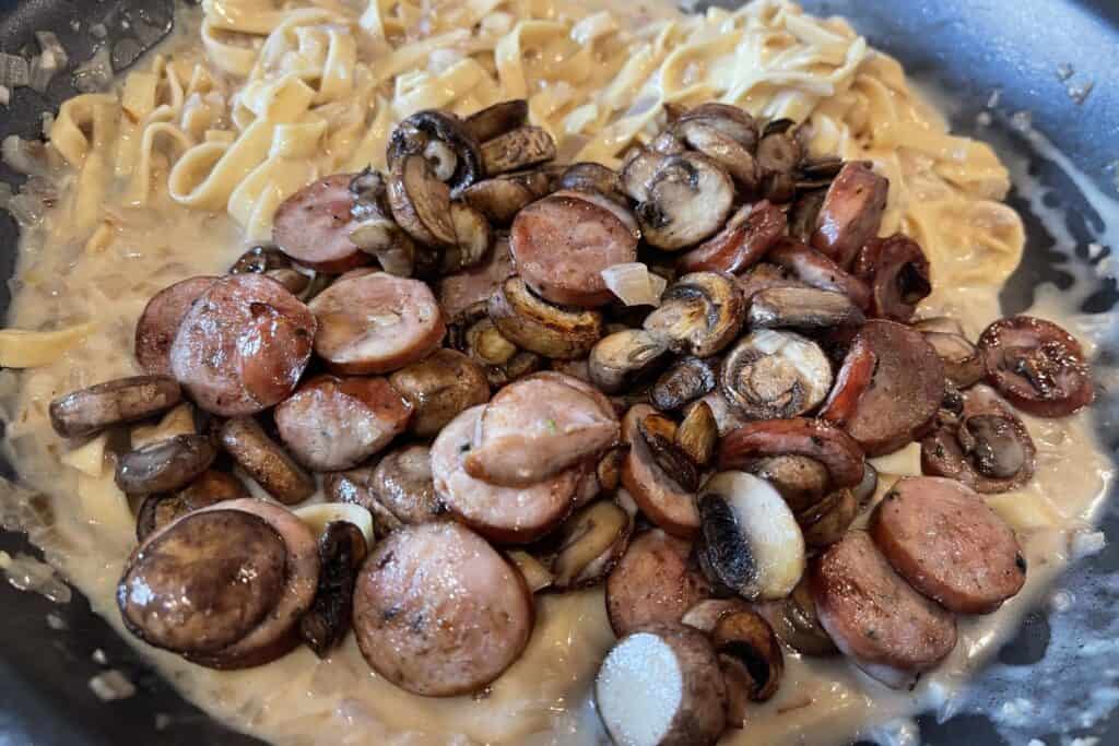 browned sausage and mushrooms in the pan with the pasta