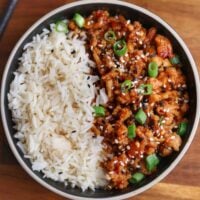 black bowl with rice and firecracker ground chicken topped with green onion and toasted sesame seeds