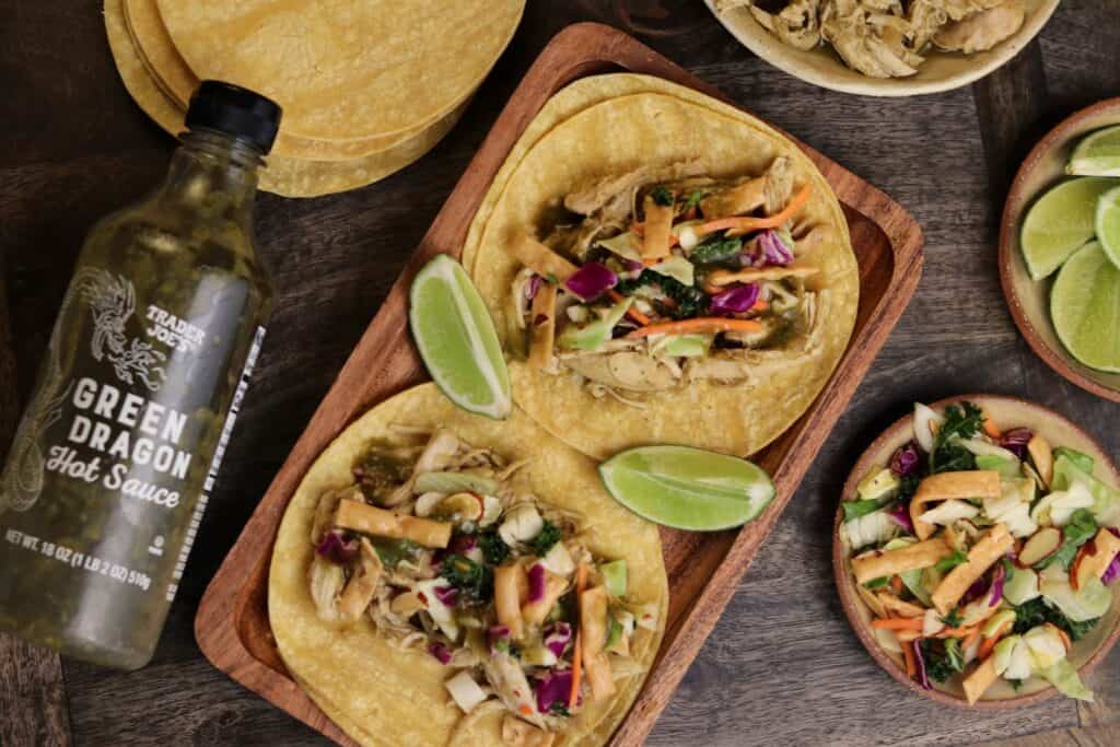 two tacos with chicken and Asian slaw on a wooden plate