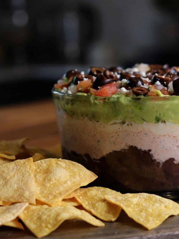 bowl of layer dip on a board with tortilla chips