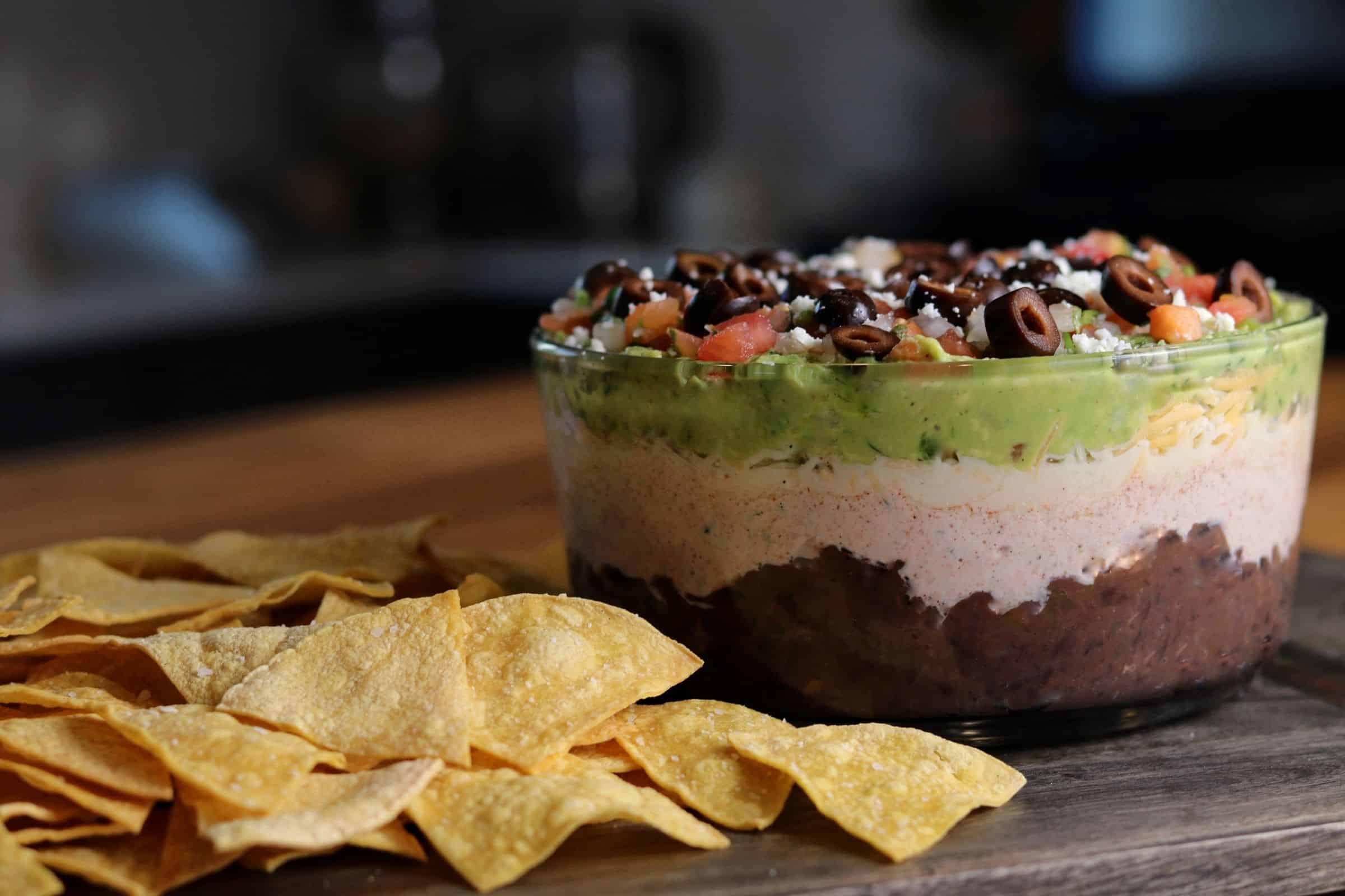 bowl of layer dip on a board with tortilla chips
