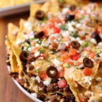 trash can nachos copycat on a plate with olives, pico de gallo, and queso fresco on top