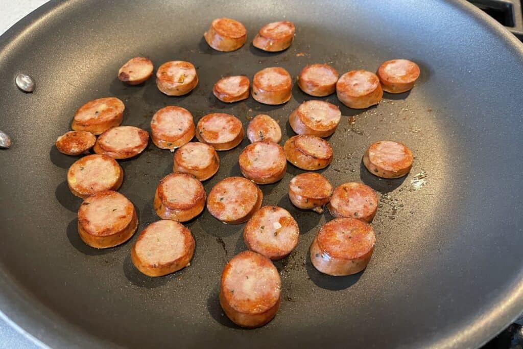 sliced chicken sausage rounds browning in a skillet