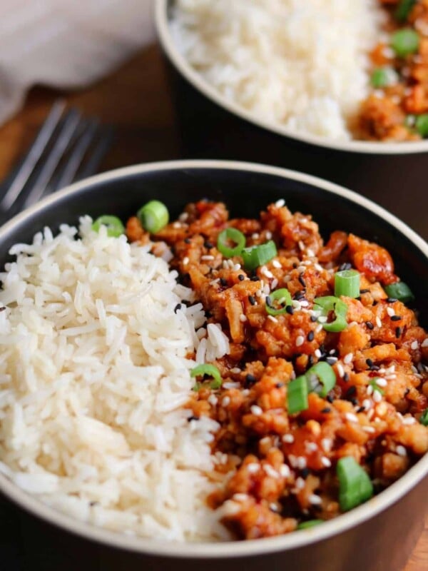 two bowls of firecracker ground chicken with rice garnished with scallions and sesame seeds