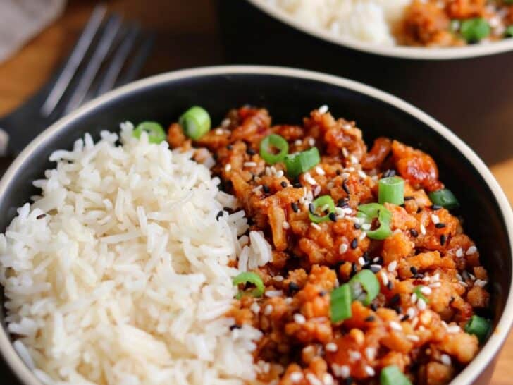 two bowls of firecracker ground chicken with rice garnished with scallions and sesame seeds