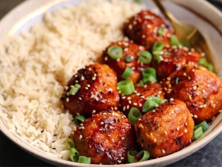firecracker chicken meatballs in a bowl with basmati rice, toasted sesame seeds, and green onion