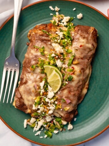 two enfrijoladas on a green plate garnished with jalapeño salsa