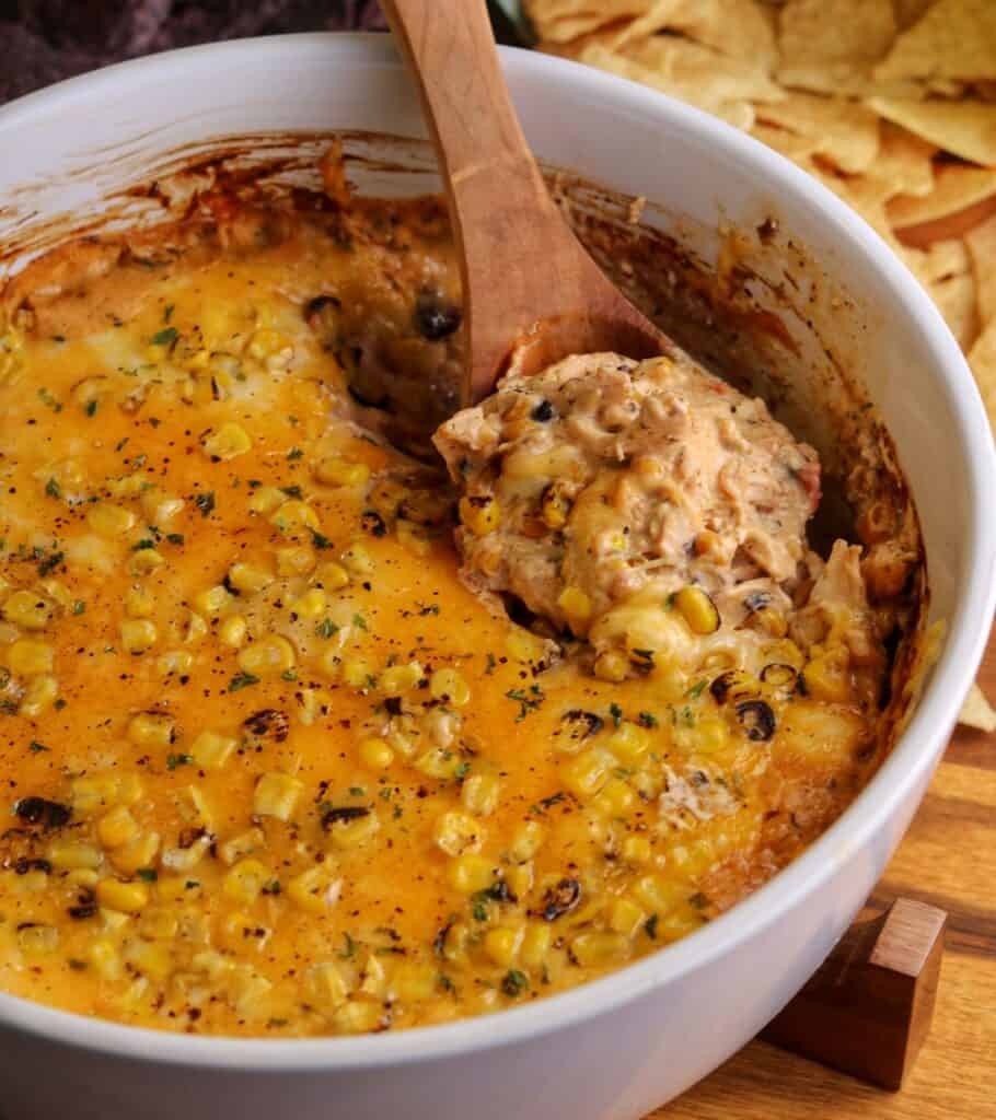 a white bowl with cheese topped cowboy caviar chicken dip and tortilla chips on the side