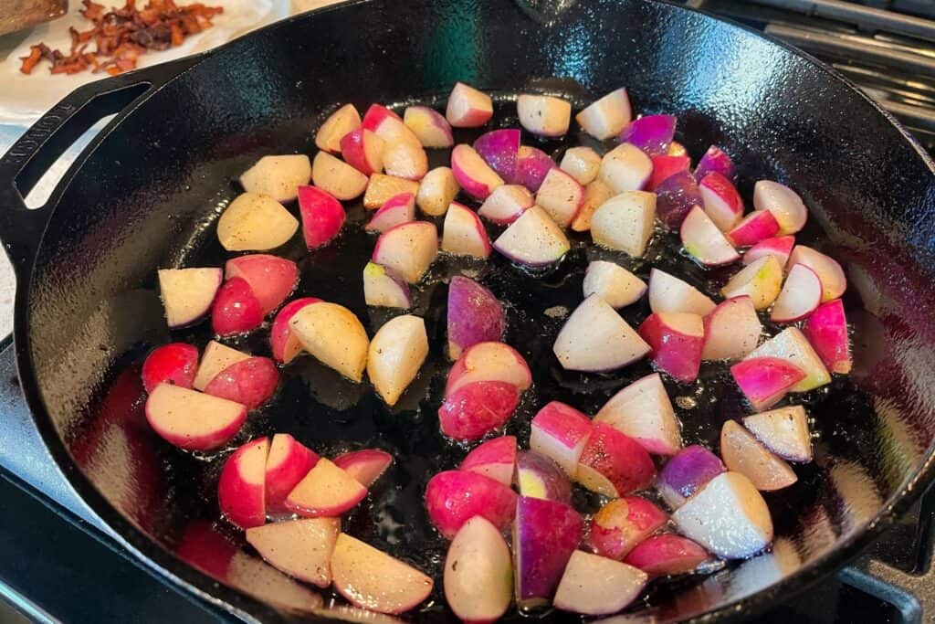 radishes cooking in a cast iron skillet with rendered bacon grease