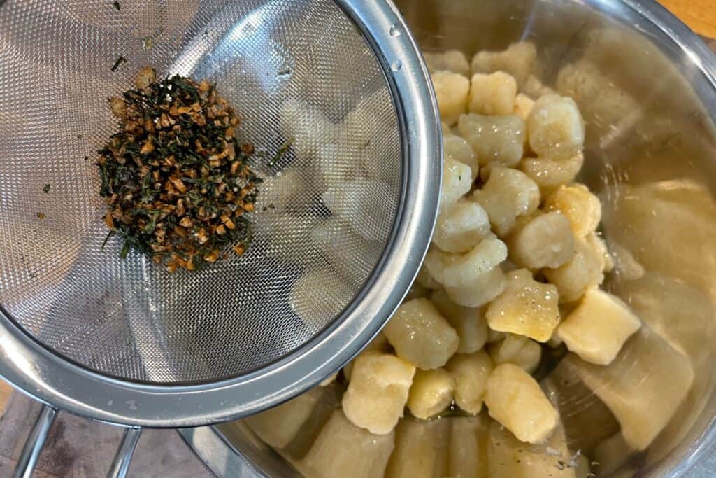 mesh strainer with garlic and rosemary over microwaved cauliflower gnocchi