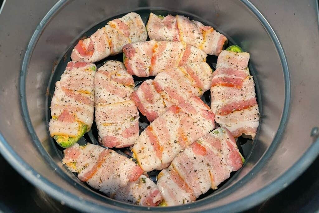 bacon wrapped jalapeño poppers in an air fryer basket before cooking