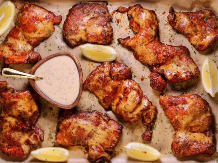 smoked chicken thighs on a baking sheet with Alabama white sauce and lemon wedges