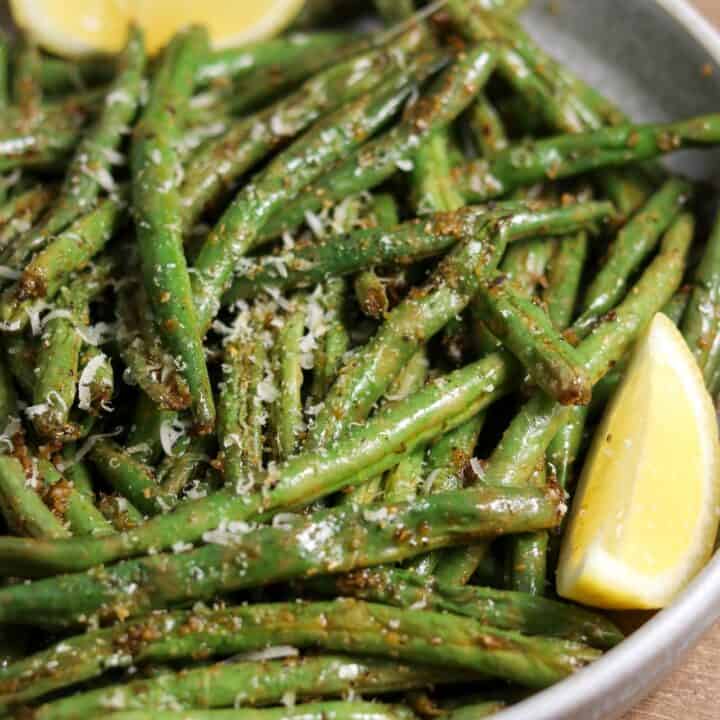 air fryer green beans in a bowl with grated parmesan and lemon wedges