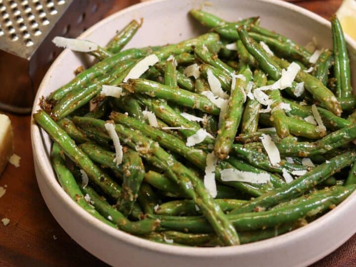 green beans in a bowl with grated parmesan and a lemon wedge