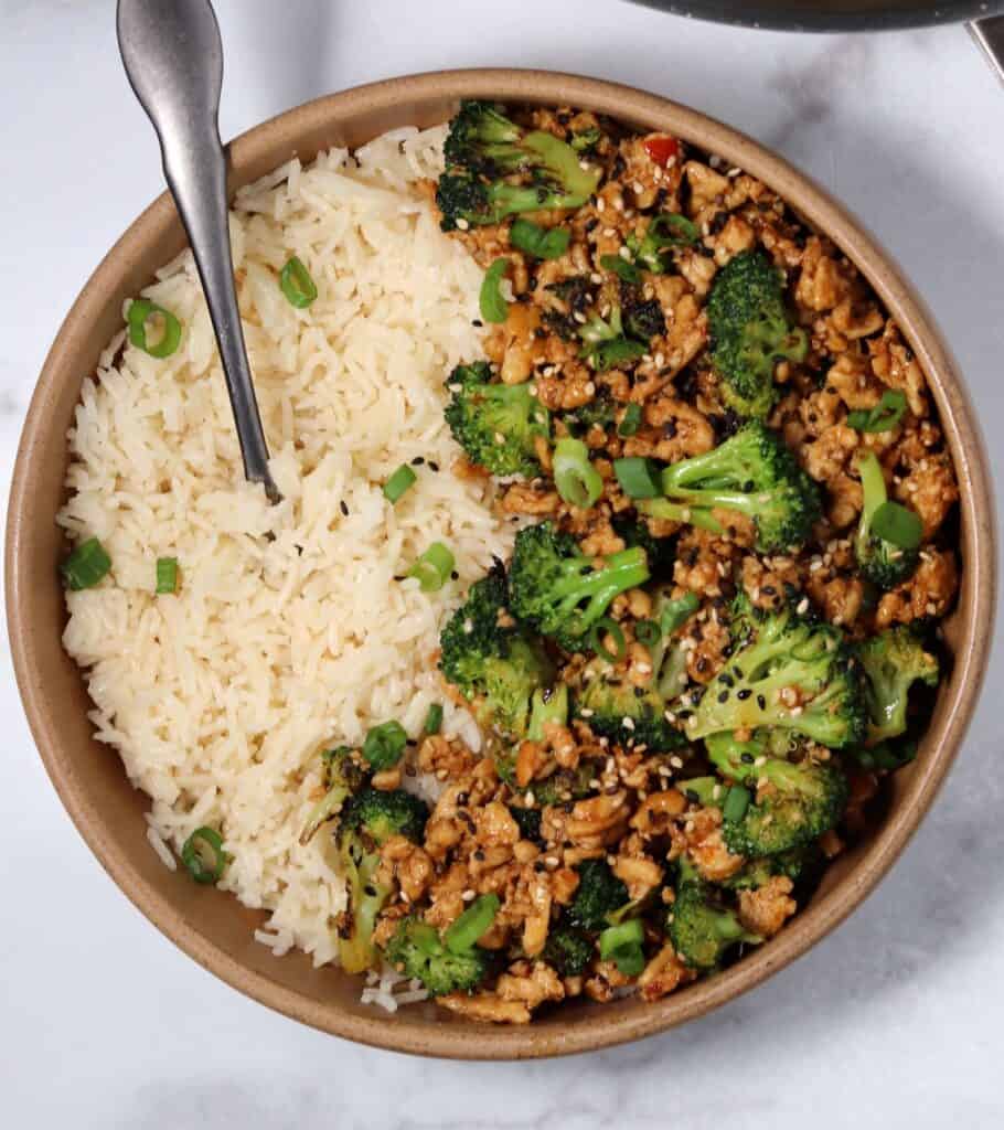 chicken and broccoli with sesame seeds in a brown bowl with rice