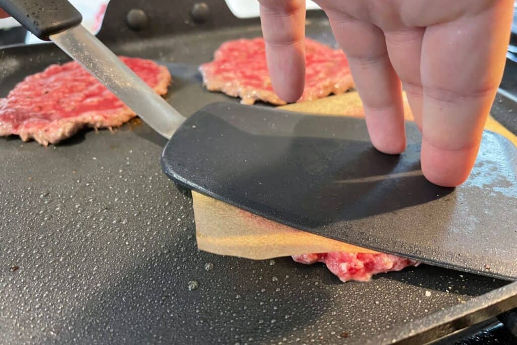 cooking smash burgers on a griddle with parchment paper