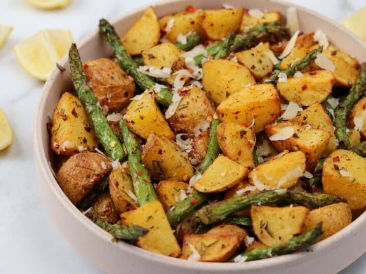 air fried asparagus and potatoes in a bowl with parmesan and lemon wedges