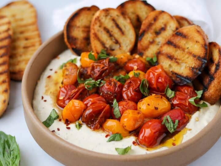 whipped feta dip topped with roasted tomatoes in a bowl with grilled bread