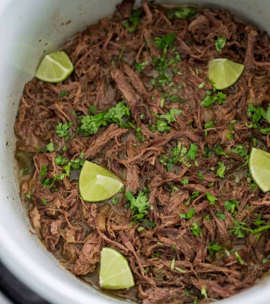 pulled beef with cilantro and lime wedges in a slow cooker pot