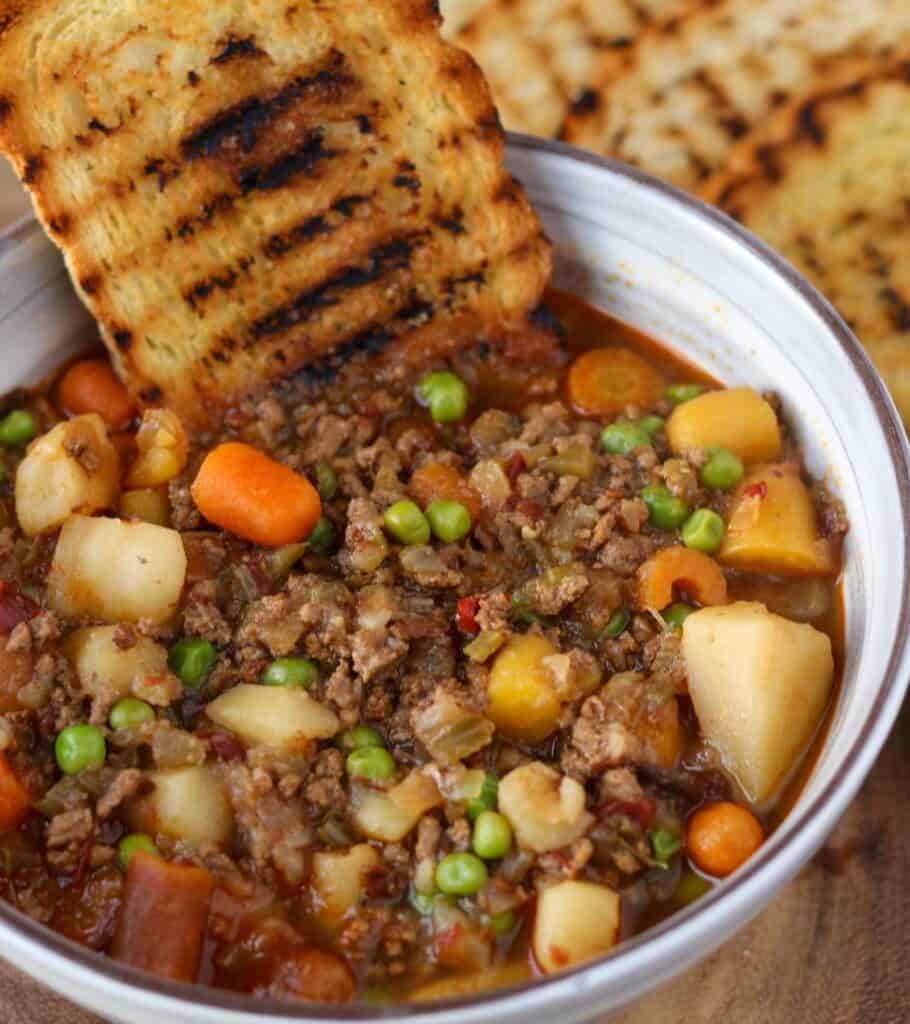 bowl of vegetable beef soup with a piece of grilled bread