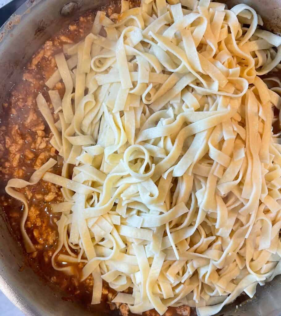 cooked carba-nada noodles in a skillet with cooked ground chicken and spicy peanut sauce