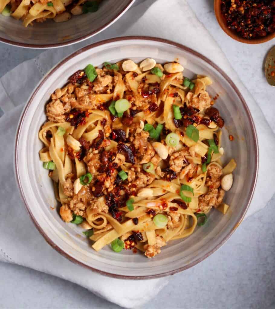 dan dan noodles in a bowl with chili crisp, scallions, and chopped peanuts