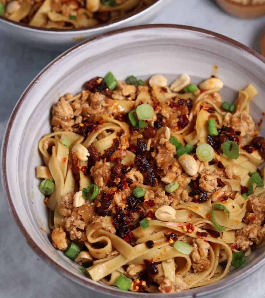 finished Dan Dan Noodles in a bowl with scallions, toasted peanuts, and chili crisp