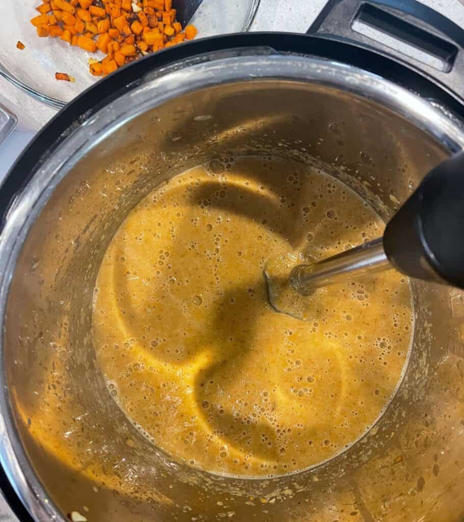 immersion blender in the Instant Pot blending the roasted vegetables into cauliflower soup