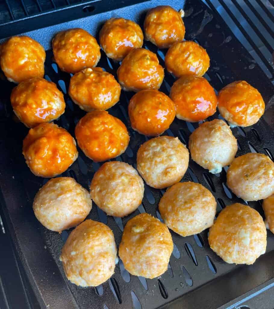 brushing half the meatballs with buffalo sauce in the Traeger