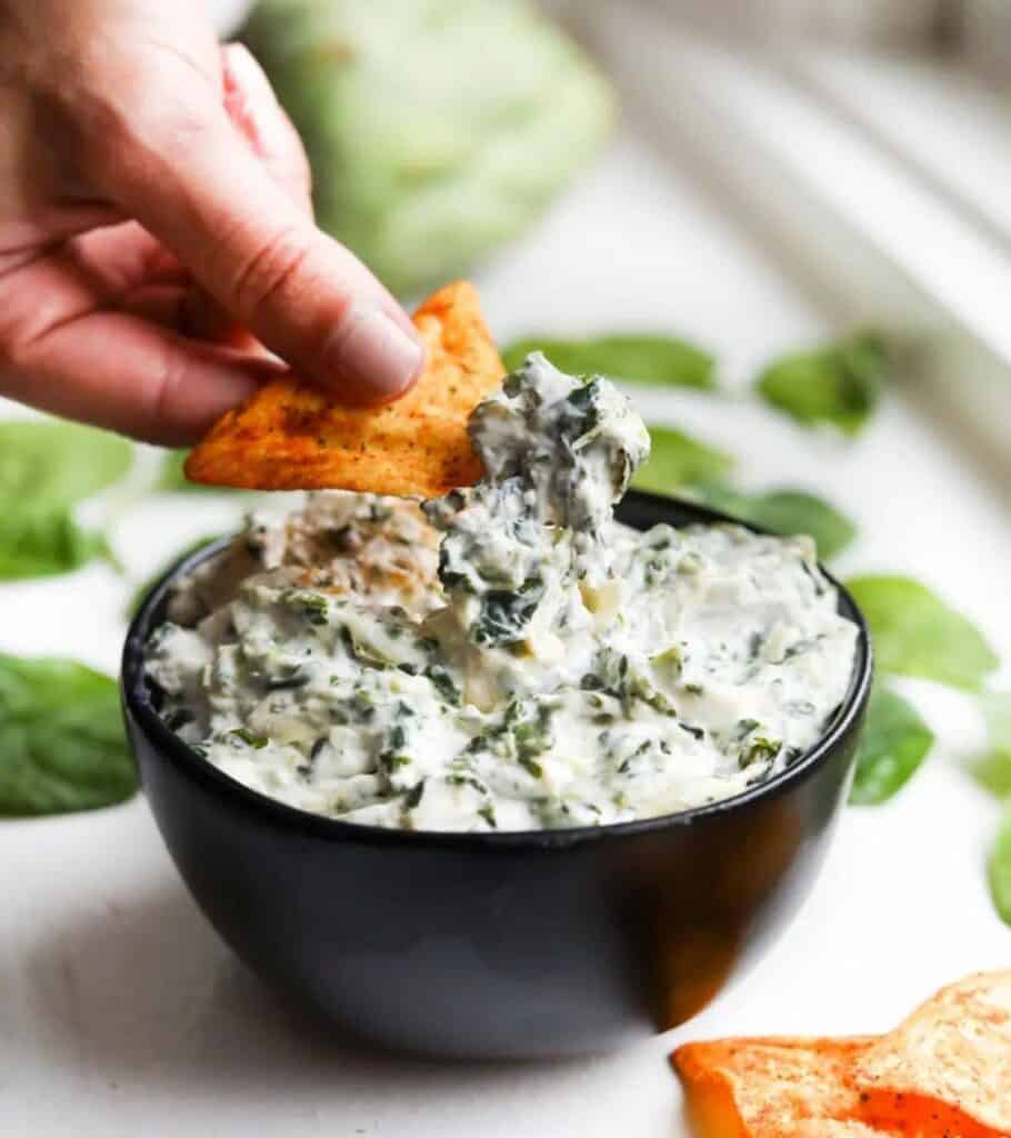 dipping a chip in spinach and artichoke dip