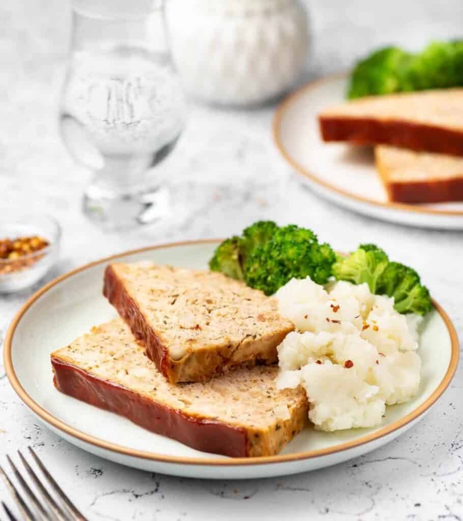 slices of chicken meatloaf on a plate with mashed potatoes and broccoli