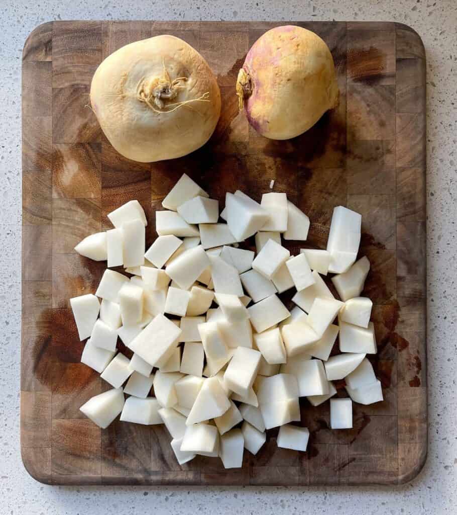 chopped turnips on a cutting board with two whole turnips