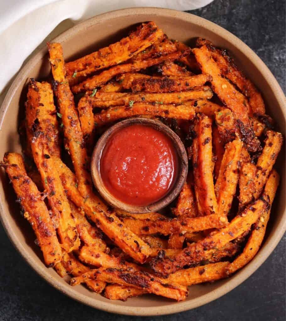 roasted carrot sticks in a brown bowl with a small bowl of ketchup