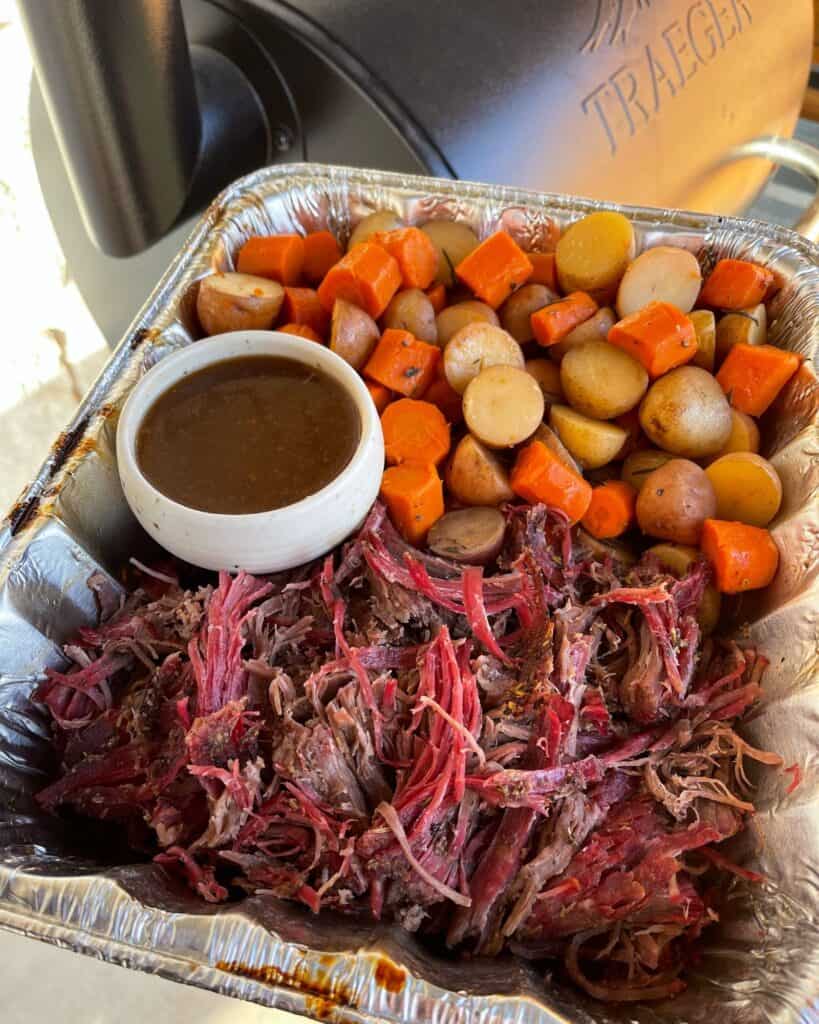 a tray of smoked pot roast with a bowl of gravy by the Traeger