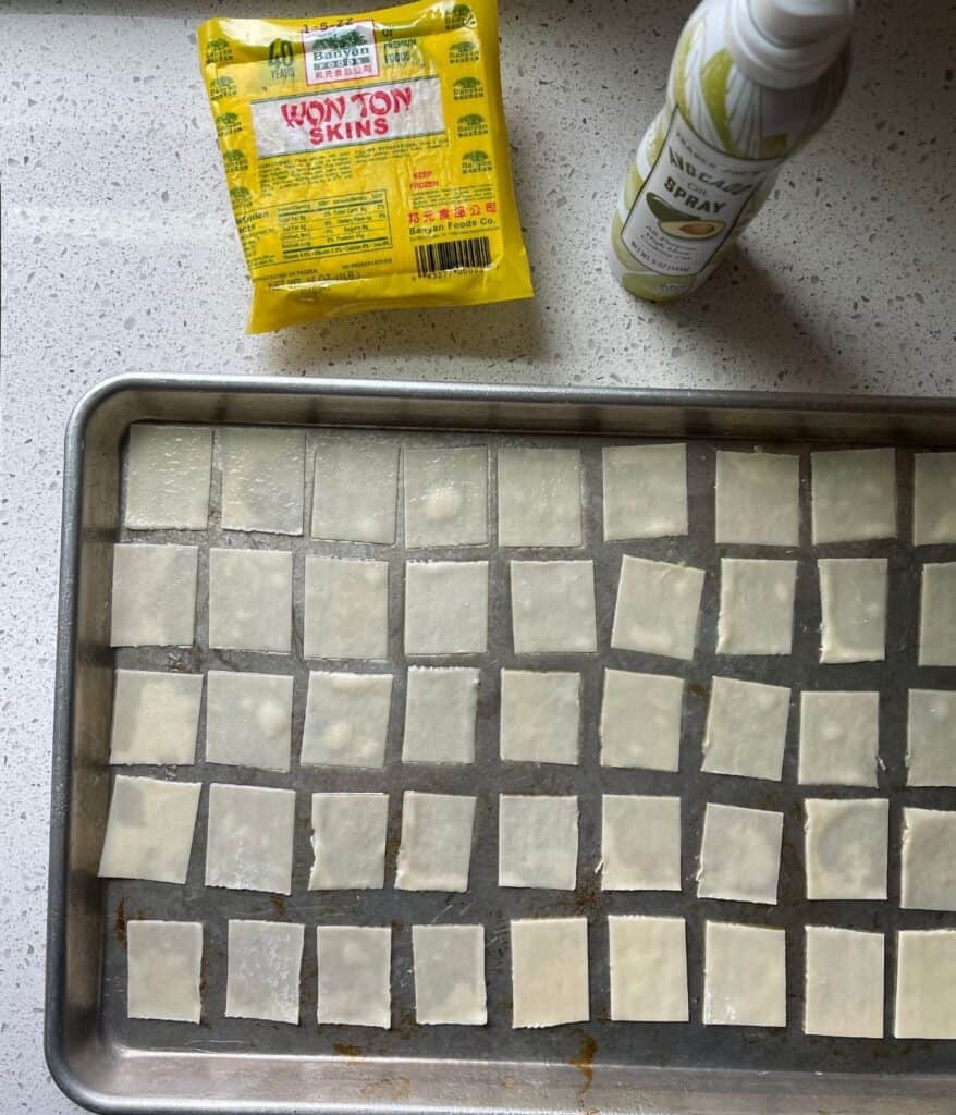 wonton wrappers cut into chips on a sheet pan with avocado oil spray
