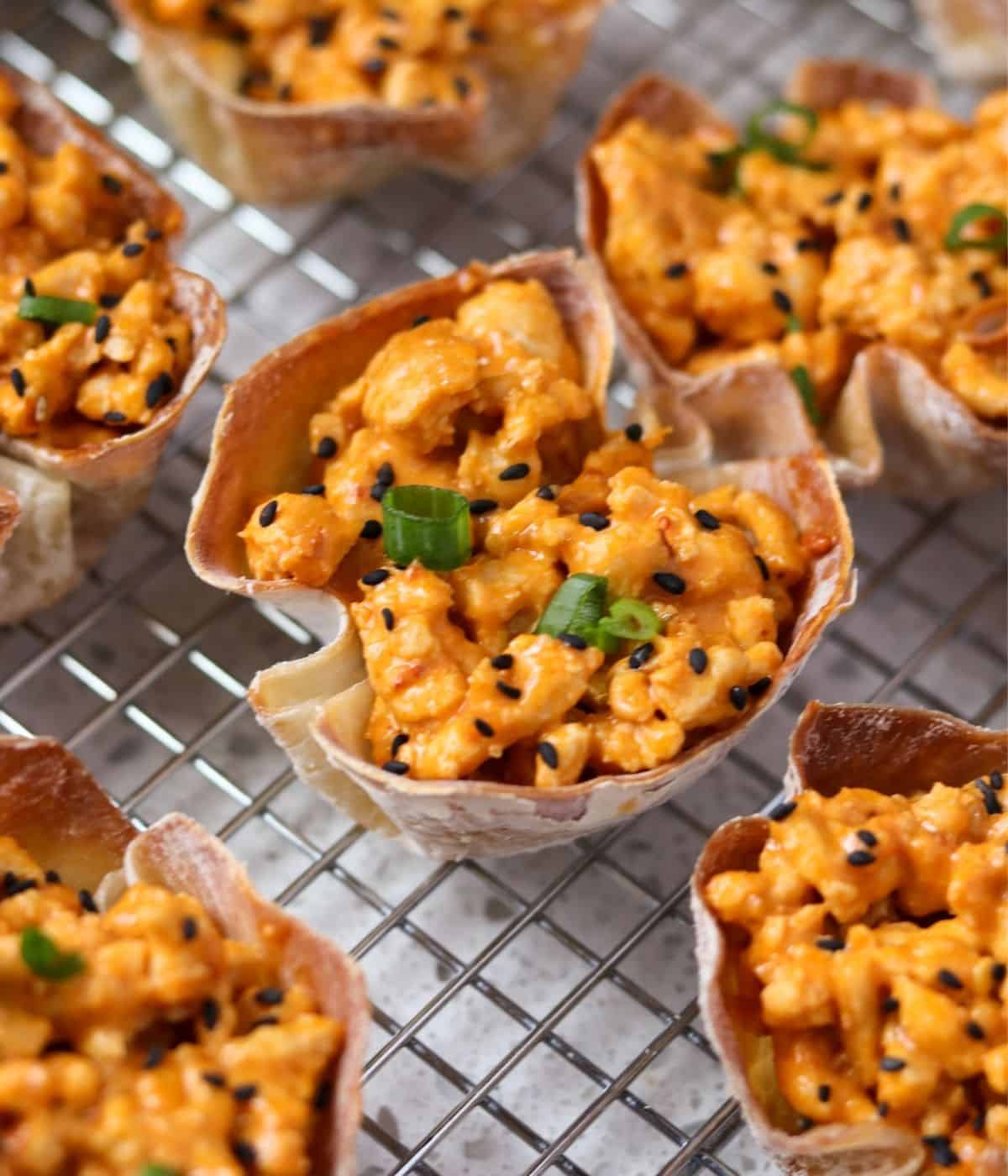 bang bang chicken wonton cups on a wire rack topped with sesame seeds and green onion