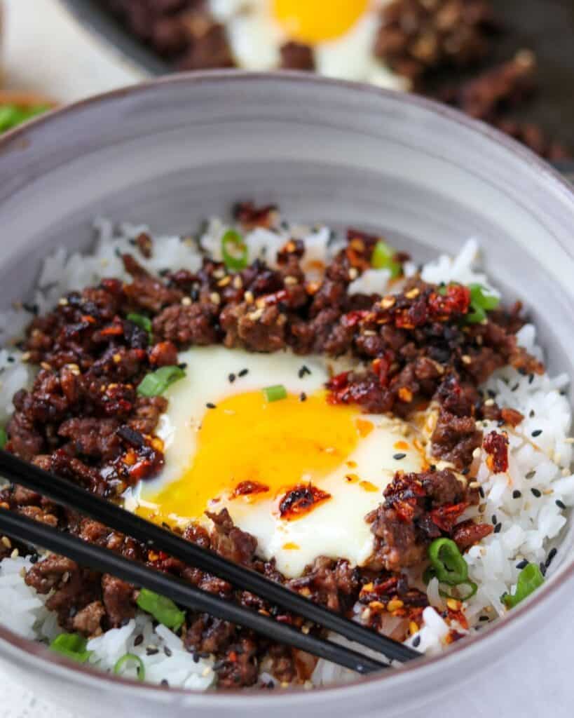ground beef with a chili oil fried egg on top of rice topped with green onion and sesame seeds