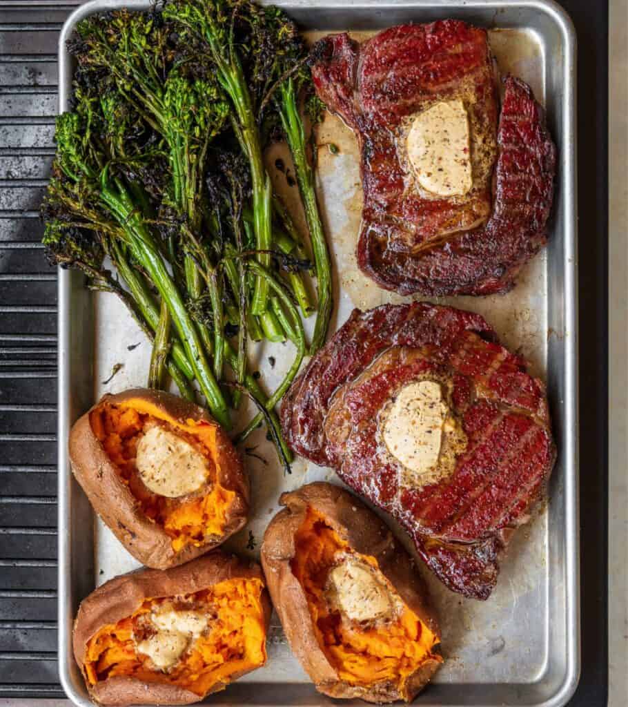 two reverse seared steaks on a Traeger with grilled broccolini and baked sweet potatoes