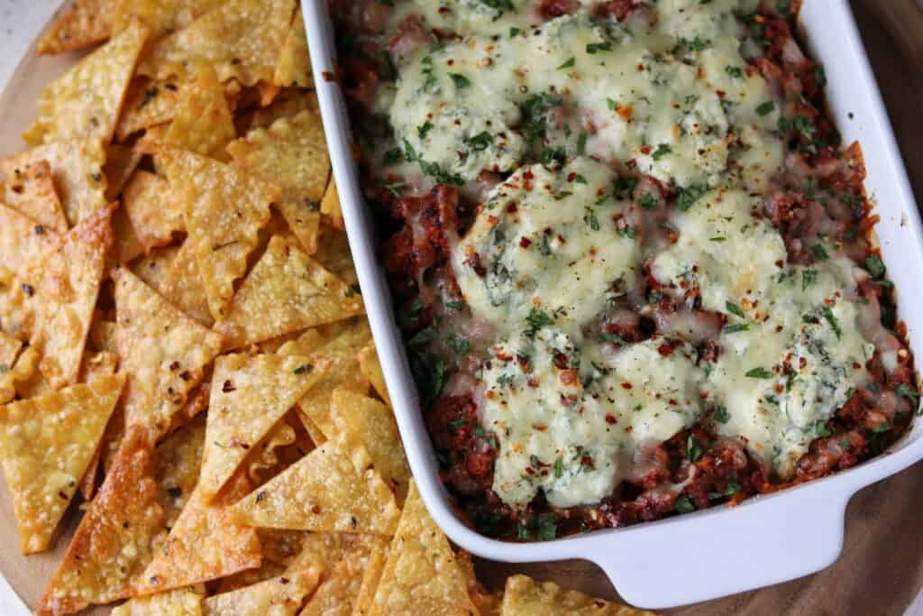 baked pasta chips beside a baking dish filled with lasagna dip