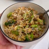 holding a bowl of ground turkey and broccoli orzo topped with grated parmesan cheese and red pepper flakes