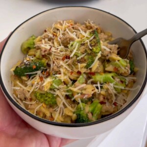 holding a bowl of ground turkey and broccoli orzo topped with grated parmesan cheese and red pepper flakes