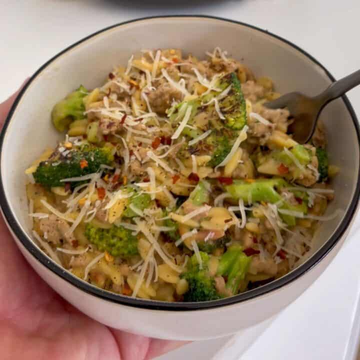 holding a bowl of ground turkey and broccoli orzo topped with grated parmesan cheese and red pepper flakes