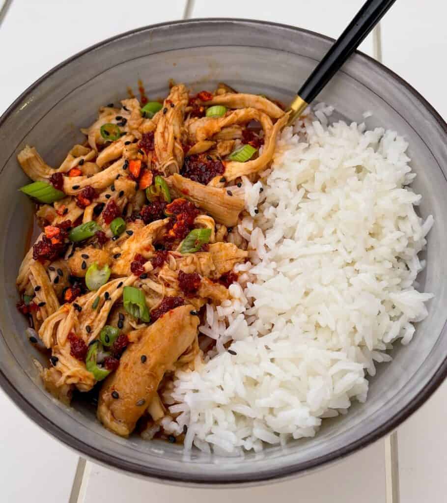 firecracker chicken thighs in a bowl with rice and garnished with scallions and chili crisp