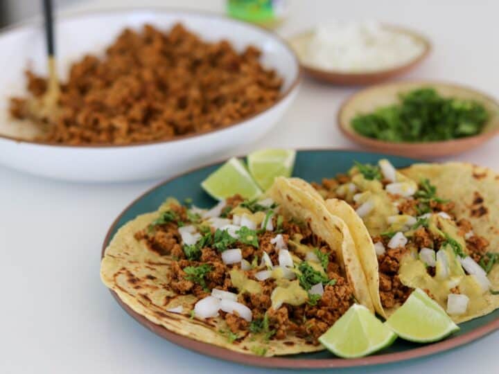 two ground pork tacos with a bowl of ground pork taco meat