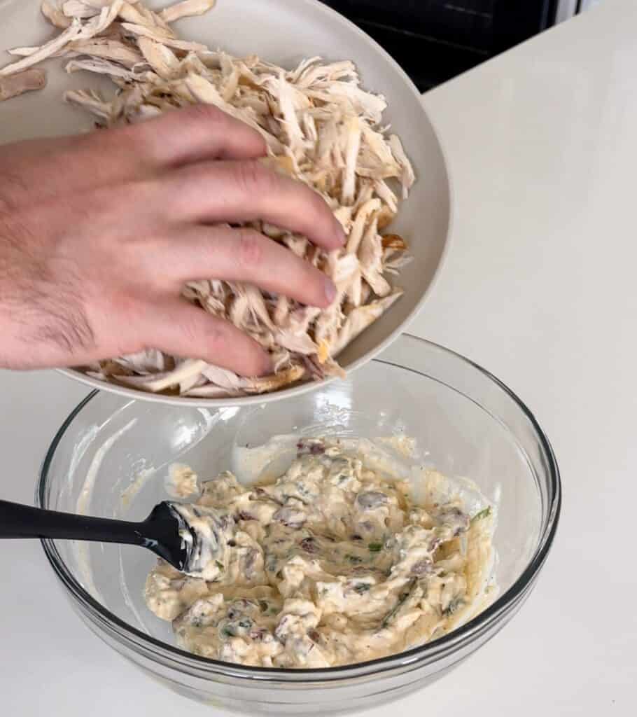 pulled rotisserie chicken going in a bowl with the creamy components