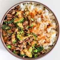 bowl of cauliflower rice and jasmine rice topped with teriyaki ground beef, scallions, sesame seeds, and yum yum sauce