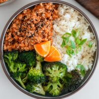 orange chicken topped with sesame seeds and served with broccoli, rice with scallions, and orange wedges