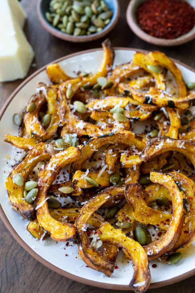 air fried delicata squash on a plate garnished with parmesan, pumpkin seeds, honey, and chile flakes