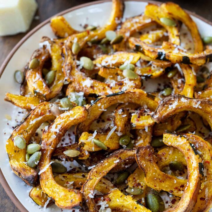 air fried delicata squash on a plate garnished with parmesan, pumpkin seeds, honey, and chile flakes