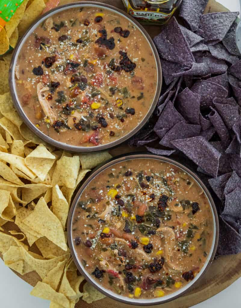 bowls of chicken taco soup garnished with cotija cheese and salsa macha surrounded by blue corn and white corn tortilla chips